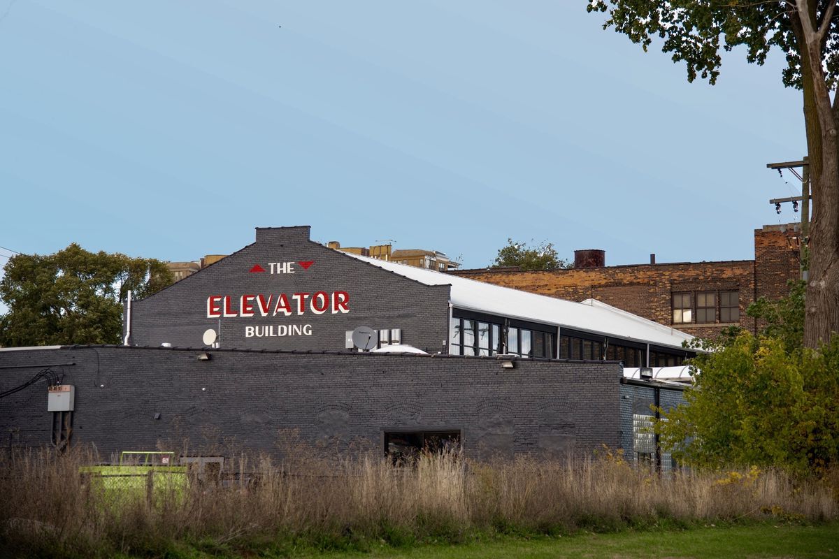 A gray-painted industrial building with a logo, painted in red and white, that says “The Elevator Building.”