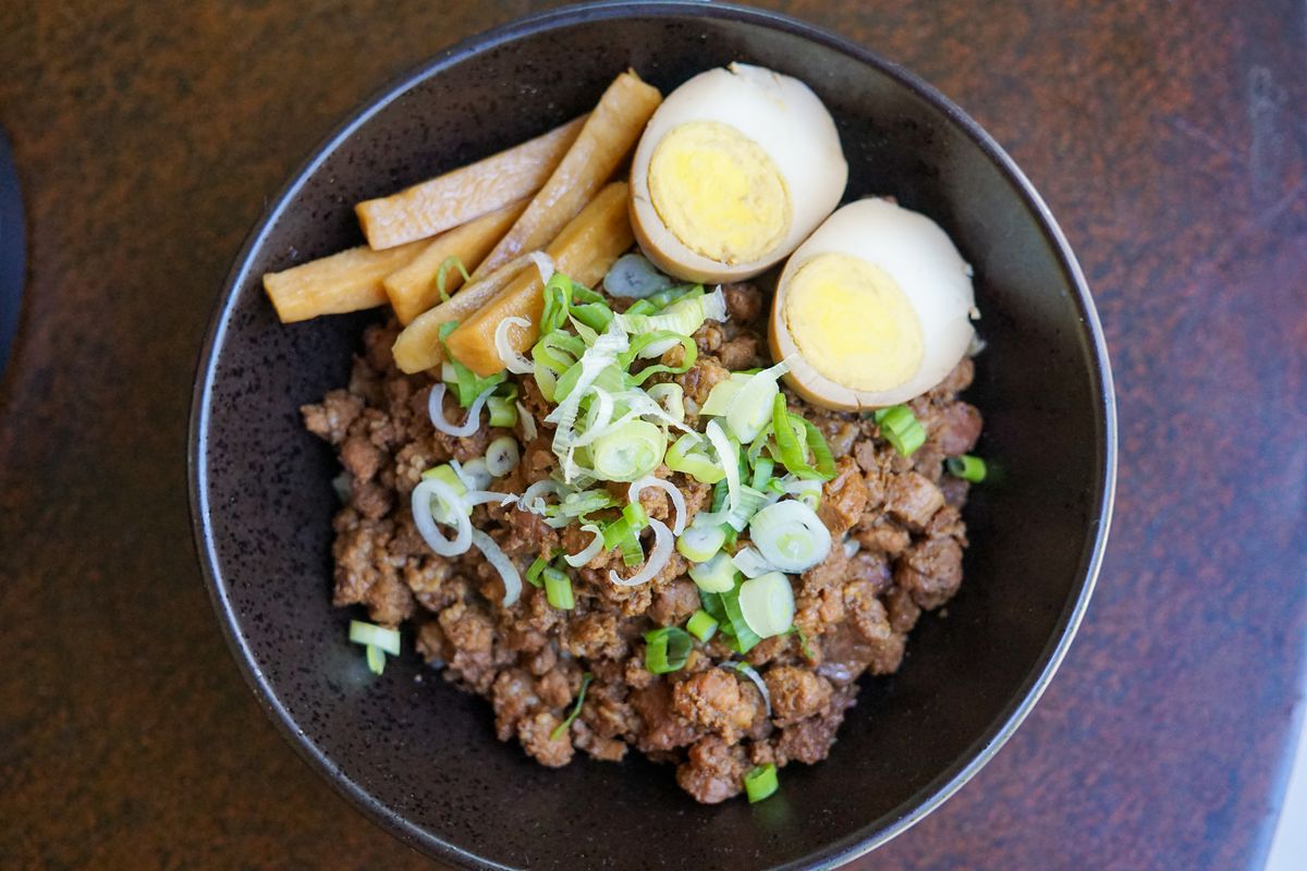 An overhead shot of clusters of meat and a cooked egg on rice in a bowl.