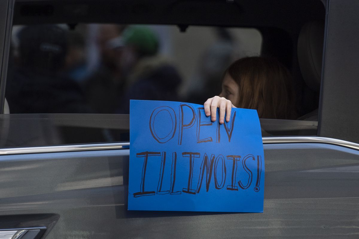A person in the backseat of a van holds up a sign the says “Open Illinois!”