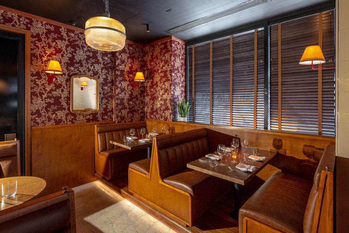 Wooden booths with dark upholstery line a lowlit dining room with red and white patterned wallpaper.