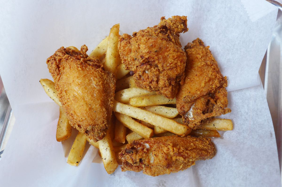 Four pieces of fried chicken on a bed of fries.