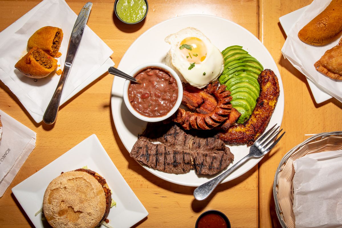 The bandeja paisa meat platter sits in the middle of the overhead photo; to the top left lies a corn and beef empanada; a spicy chicken arepa sits at the lower left-hand side of the photo