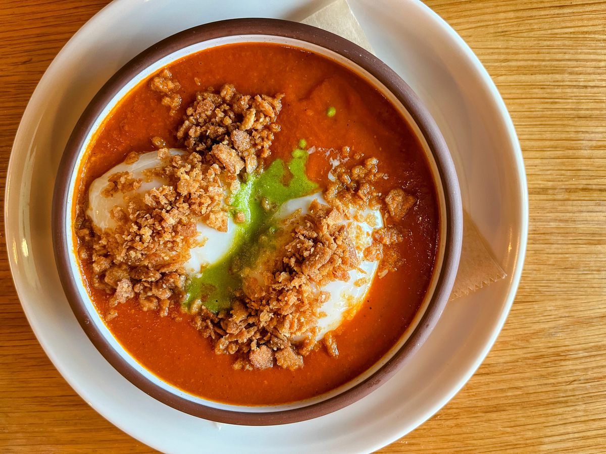 A shallow pewter bowl filled with tomato sauce, a green oil, and two poached eggs.