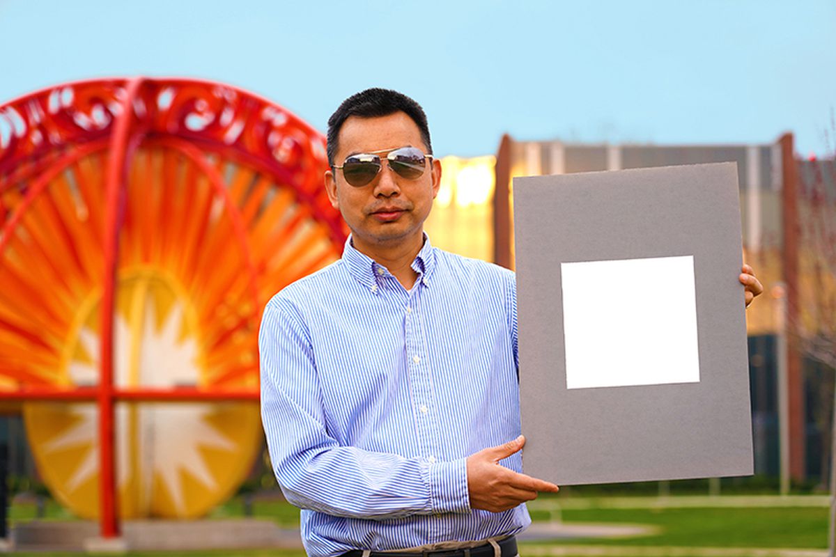 A man with sunglasses on holding up a panel with a very bright white square painted on it.
