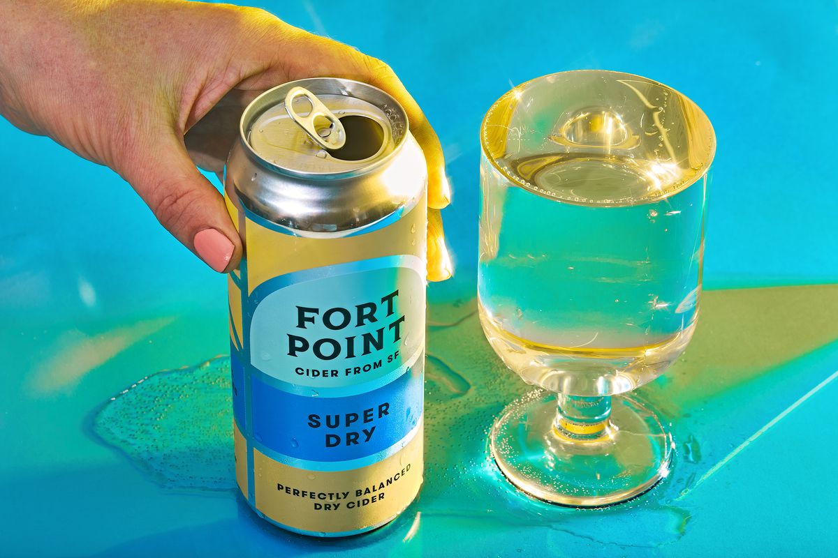 A hand reaches for a can of hard cider next to a full glass.