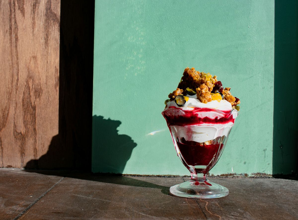 A dish that resembles an ice cream sundae is made with labneh, chickpea granola, fruit, and a drizzle of honey.