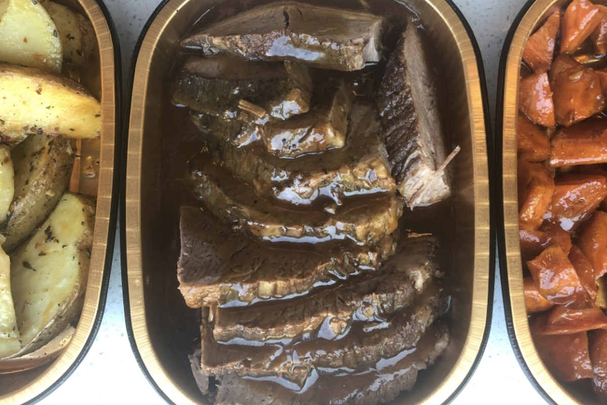 A takeout container filled with slices of braised beef brisket, covered with gravy 