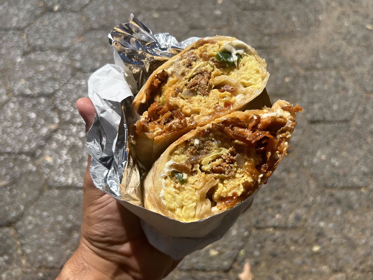 A hand holds up two halves of a burrito with chorizo, egg, and peppers.