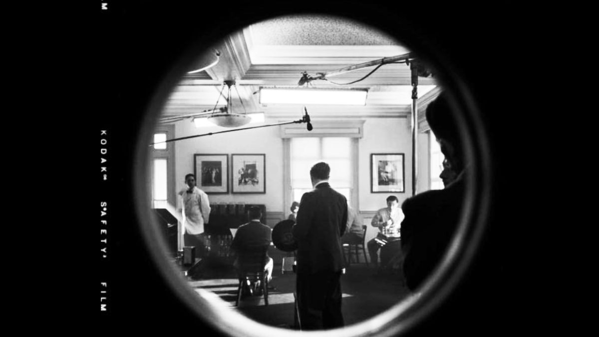 The image looks through a round window into a room where a film is being shot.