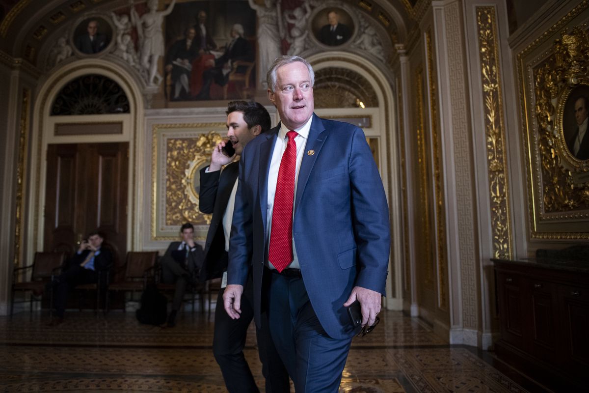 Meadows, his suit jacket open, turns to look to his left, and seems poised to speak. Behind him, the gilded arches and colorful frescos of the reception room glitter in the room’s dim light.