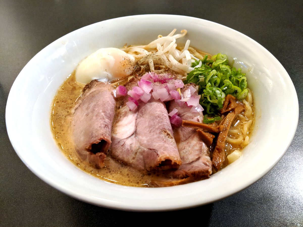 A white bowl filled with slices of pork, chopped onions, and various toppings