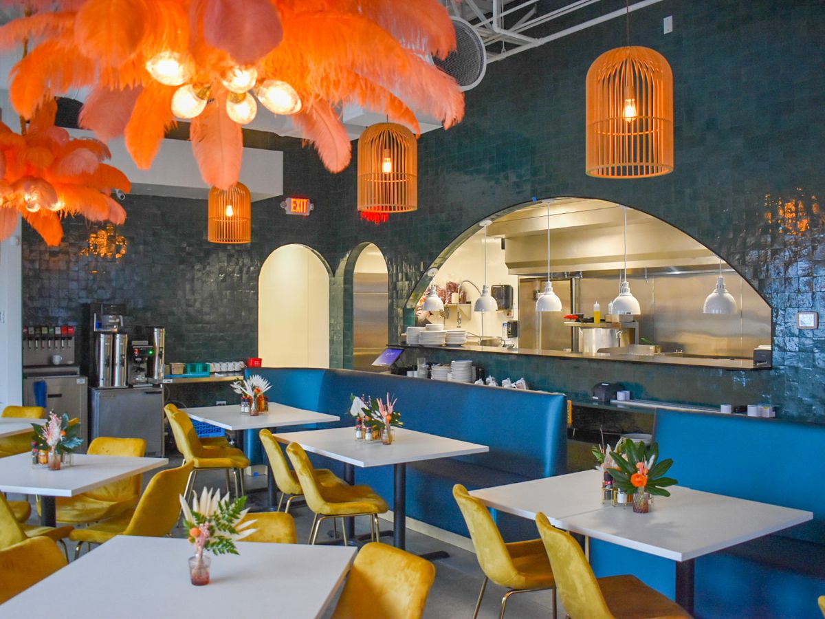 A colorful restaurant with blue walls, yellow chairs, blue benches, white tables, and orange lamps.