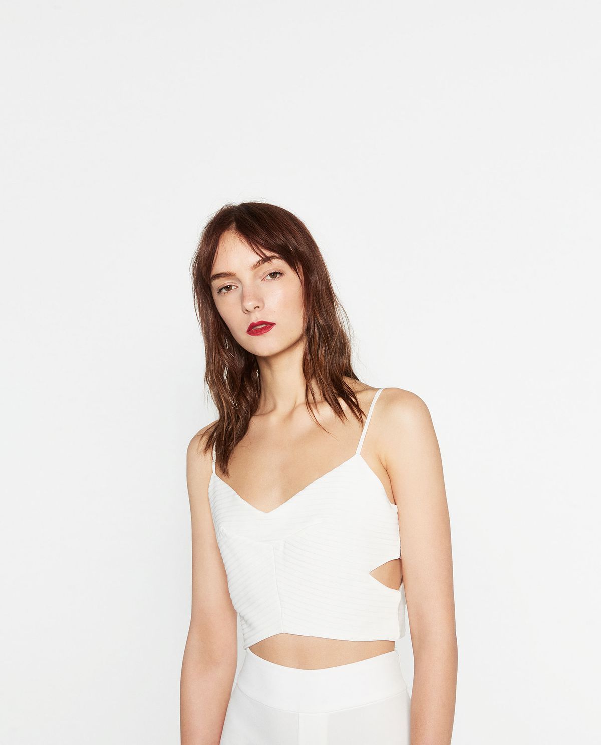A model in a white crop top with side cutouts