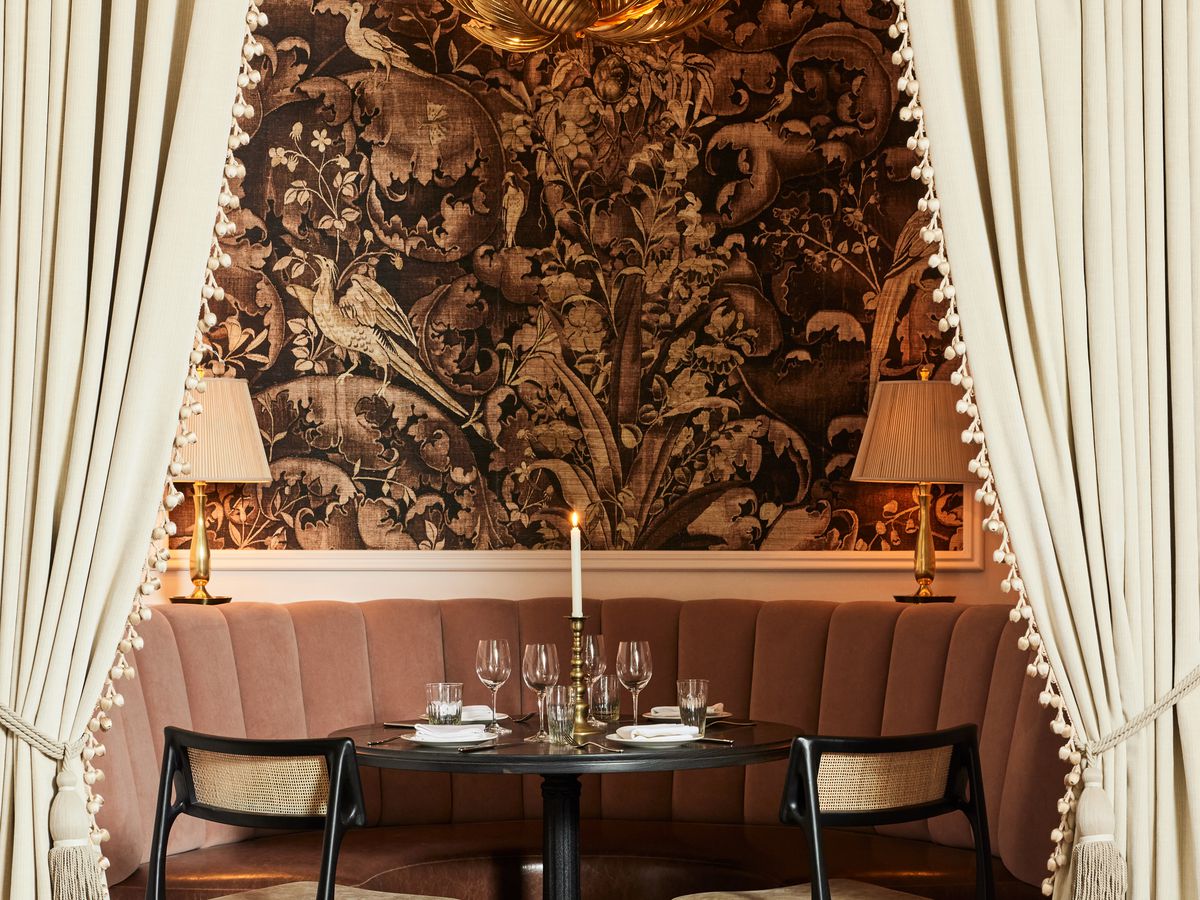A table for two is flanked by drapes and stands in front of a wall papered with an art deco print. 