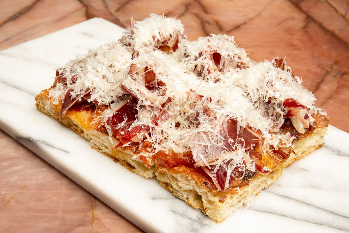 Three slices of flatbread topped with shaved Spanish ham and a snowy layer of grated cheese.
