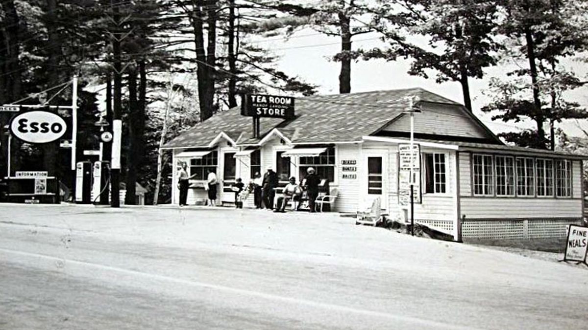 An old postcard of a gas station with a crowd hanging around out front around gas pumps