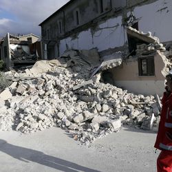An Italian Red Cross worker walks past a partially collapsed building in Accumoli, central Italy, Wednesday, Aug. 24, 2016. A devastating earthquake rocked central Italy, collapsing homes on top of residents as they slept.