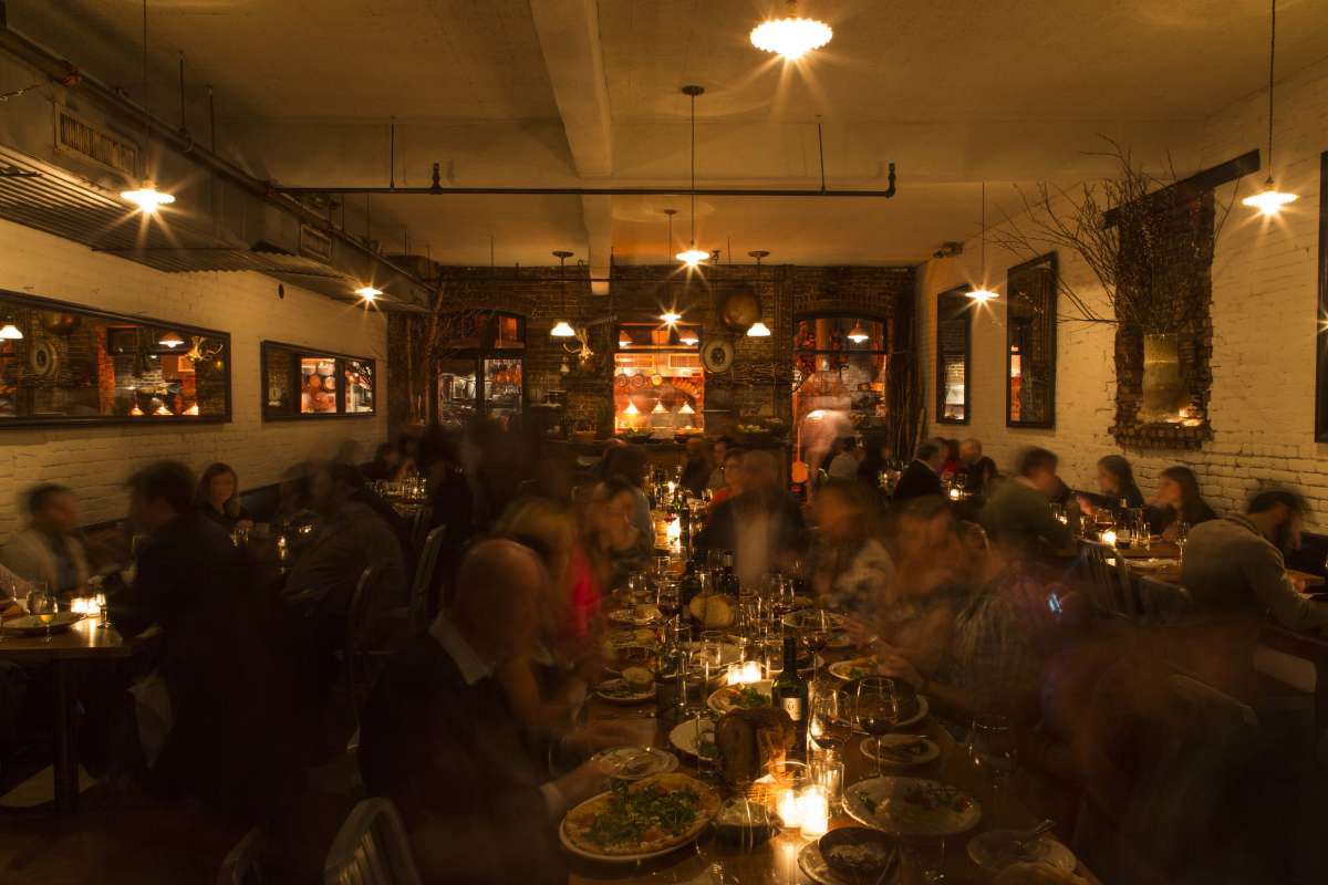 A dimly light restaurant with several people gathered around a central table, eating and talking.