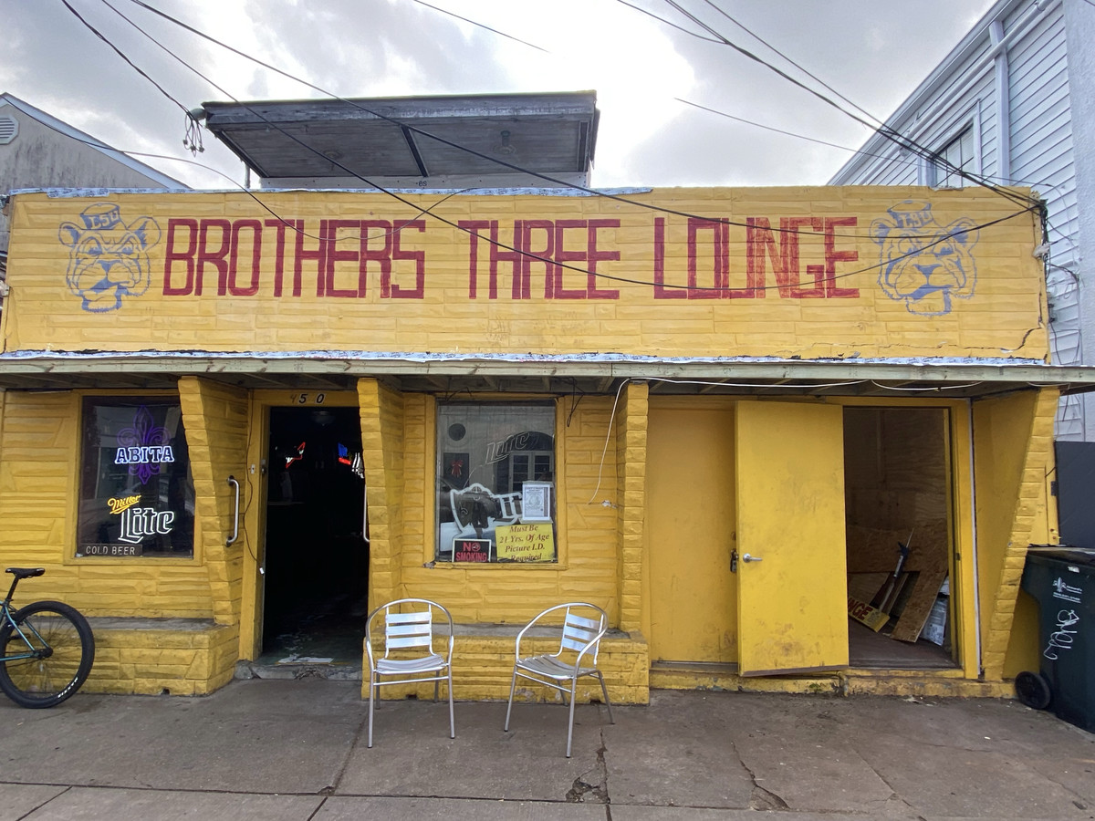 A bright yellow building with the words “Brothers Three Lounge” painted in red. 