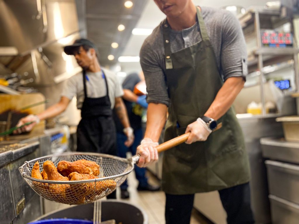 Left: A cook at Dak &amp; Bop lifts a large basket of freshly fried chicken out of the fryer. Right: A cook brushes pieces of chicken with sauce.