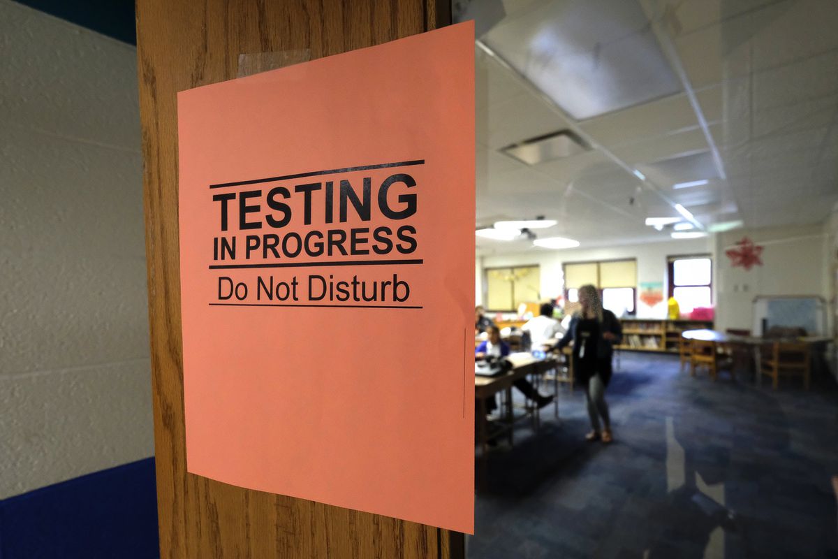 An orange sign says “testing in progress, do not disturb” as students work in the background