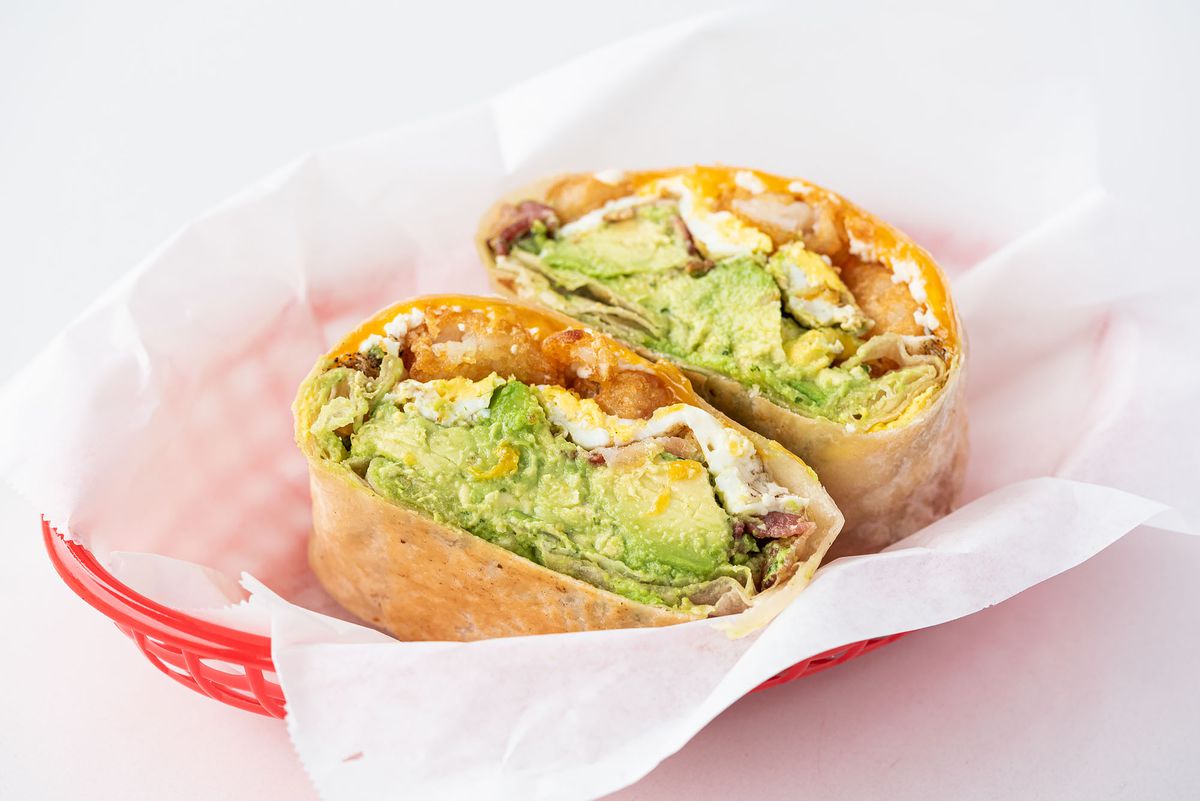 A breakfast burrito shows lots of avocado after being split in half at a daytime cafe.