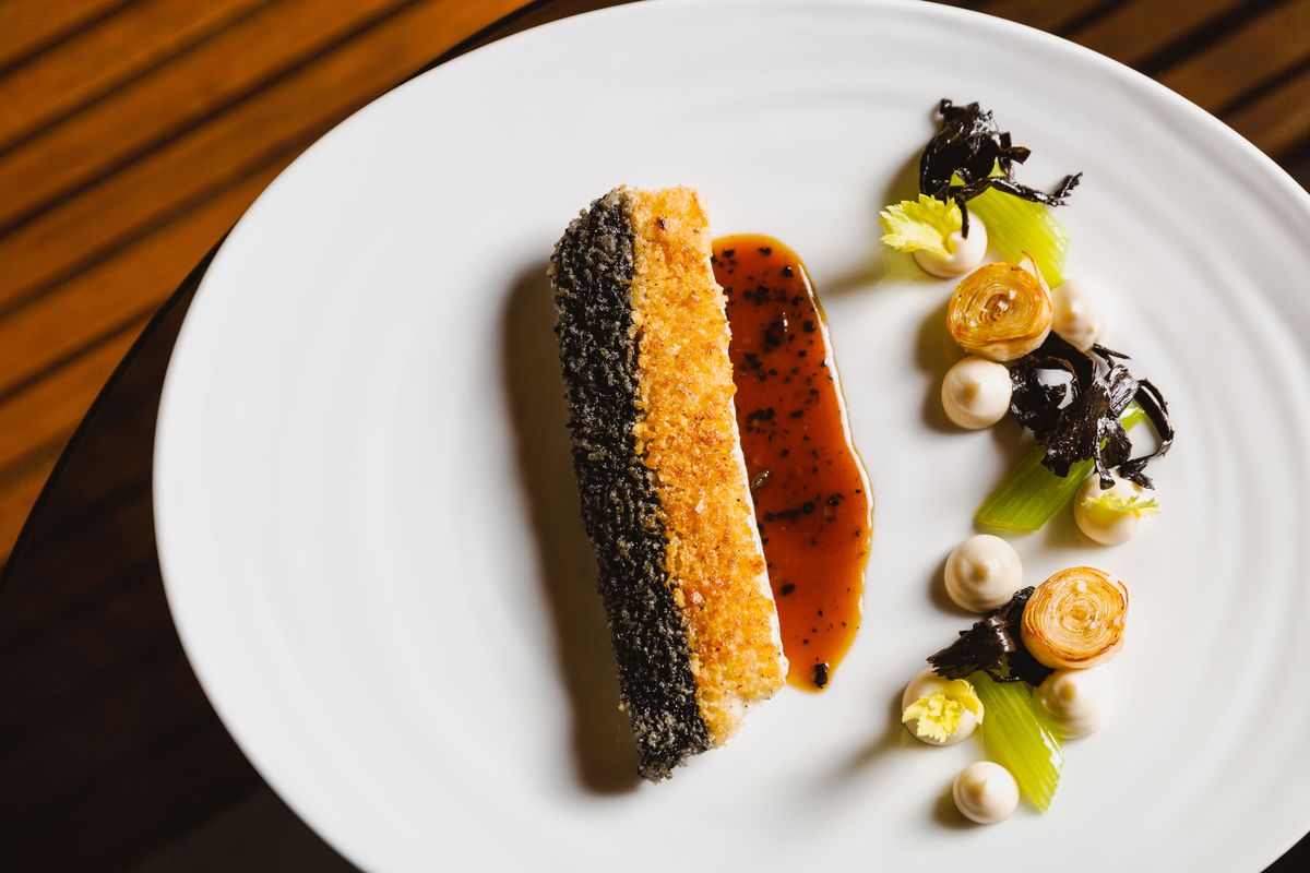 Black trumpet mushrooms and hazelnuts crust the top half of a Dover sole filet; the fish is flanked by a swath of black truffle jus