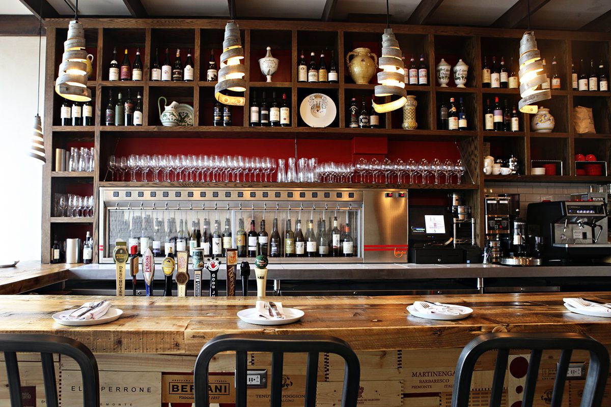 A bar stocked with tons of wine bottles, with wooden shelves and burgundy-colored paint