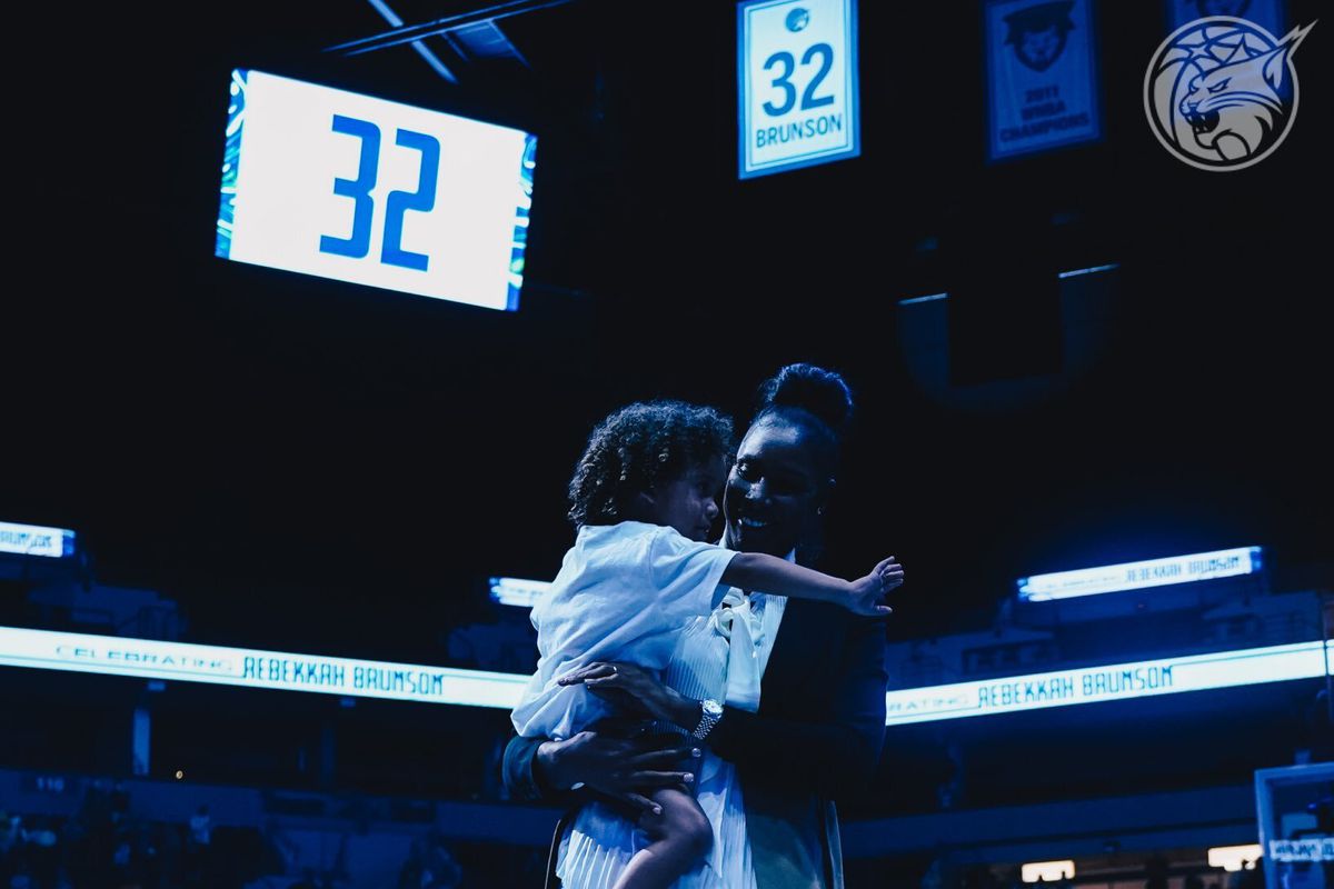 Rebekkah Brunson celebrating with her daughter in front of her jersey number being revealed.