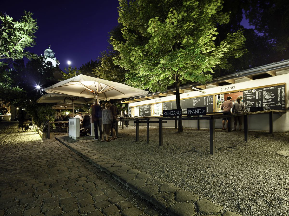 Customers at standing tables beneath umbrellas and at an outdoor bar beneath a night sky. 