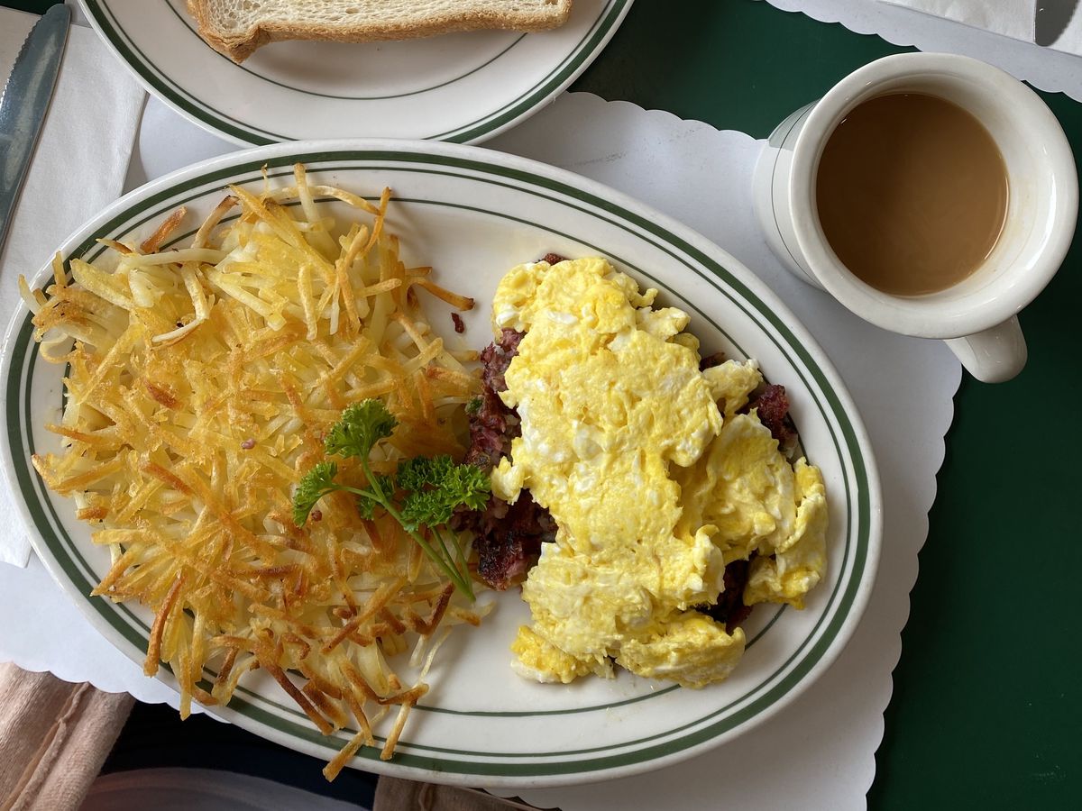 A plate of eggs, corned beef hash, and hashbrowns.