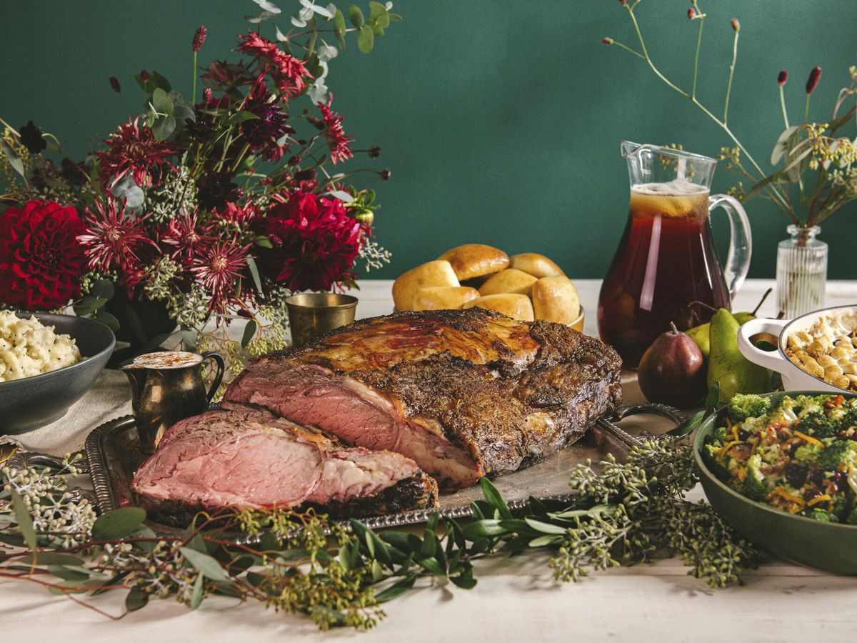 Prime rib, sides, and iced tea elaborately arranged with flowers on a white tablecloth. 