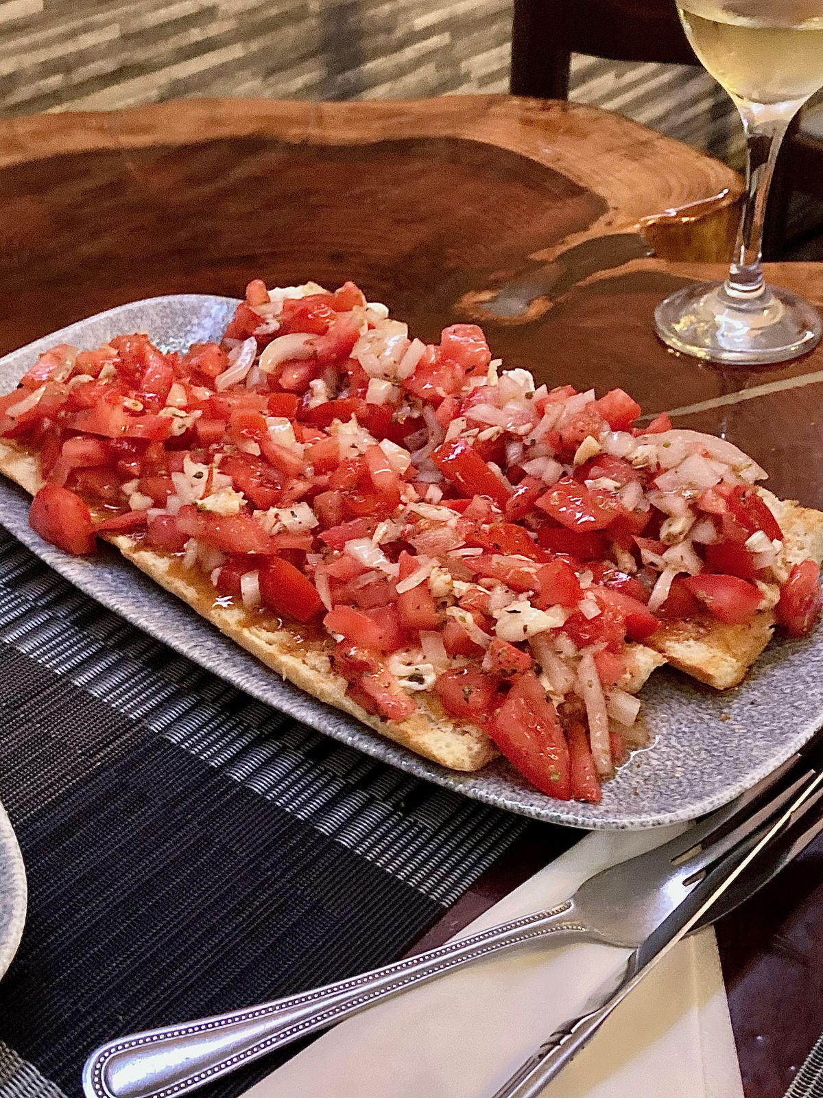 A platter of bruschetta with a glass of white wine in the background.