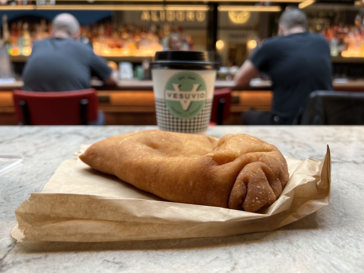 A tan panzerotti from Vesuvio sits on a marble-like counter at Moynihan Hall in front of a cardboard coffee cup