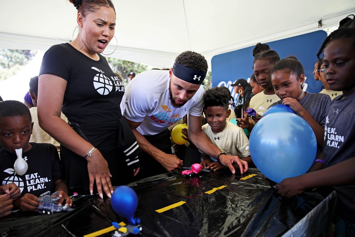Ayesha Curry and her husband, Golden State Warriors guard Stephen Curry, watch a Lego car drive with a balloon as they interact with Davon Simmons (standing beside Stephen), 9, and Kess’ya John (second from right), 9, during the launch of Eat, Play, Learn