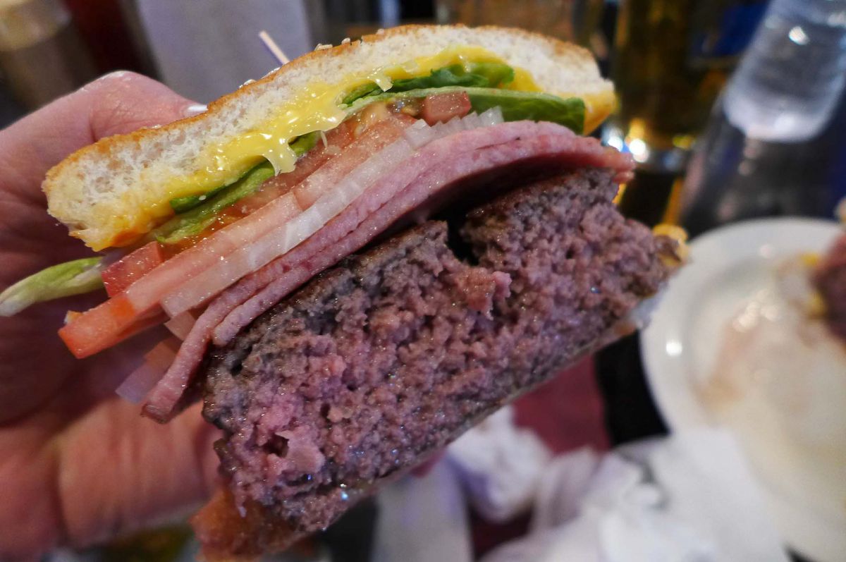 A thick burger cut in half with all the layers visible including a crumbly thick patty and two slices of ham.
