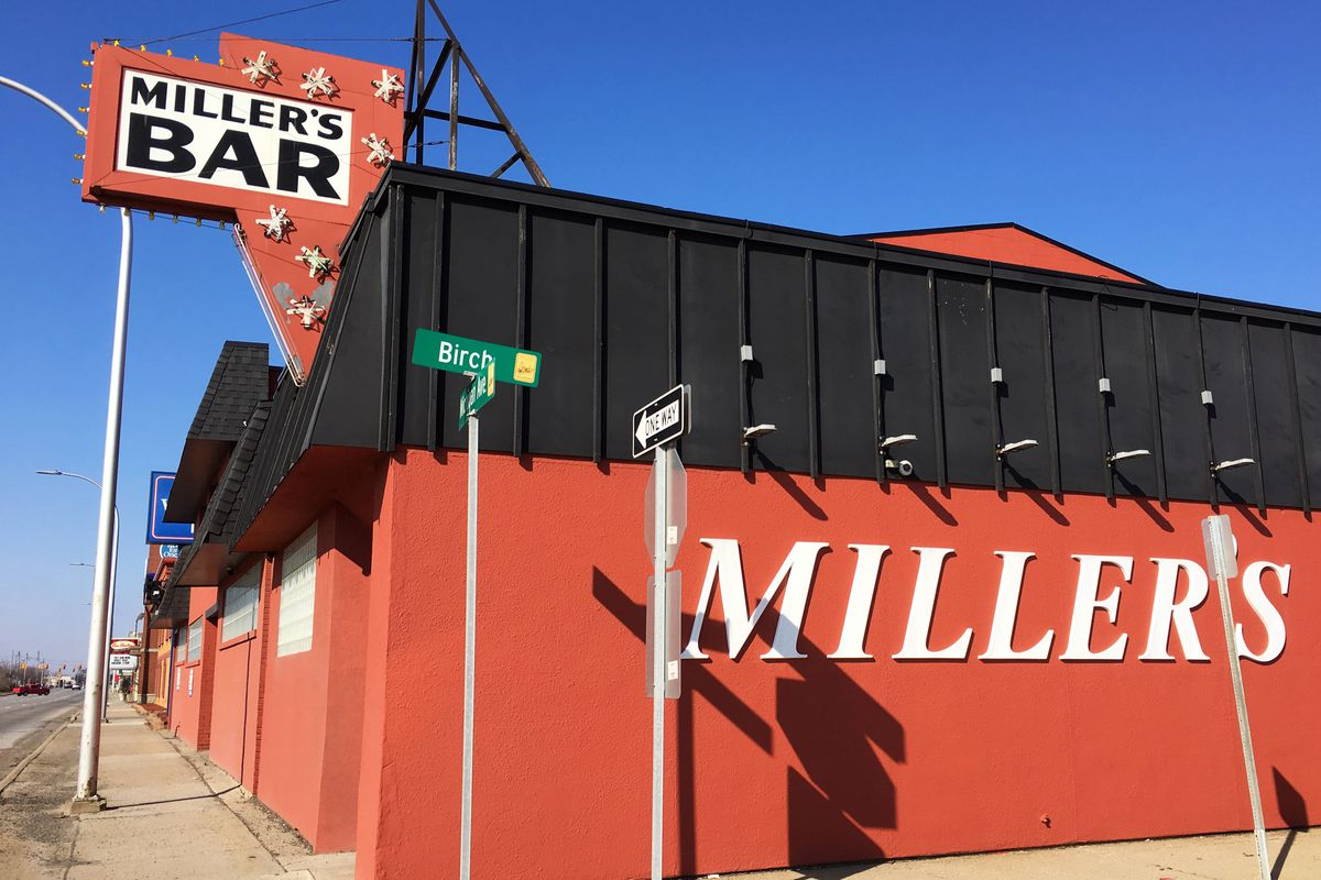 The red, brick exterior of Miller’s bar has the word Miller’s on the side of the building, and a sign on top that reads Miller’s Bar. It’s on a corner.