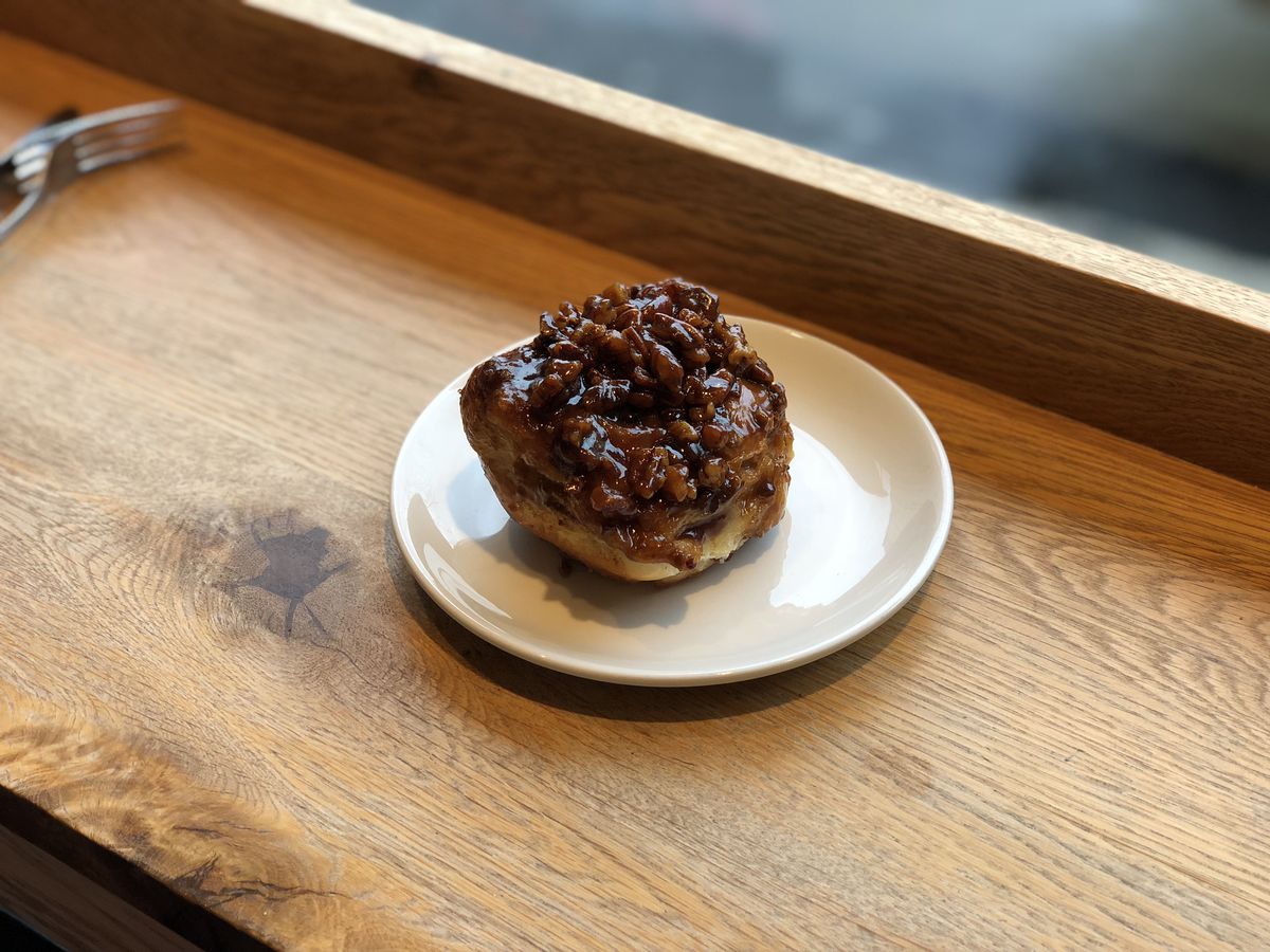 A sticky bun sits on a white plate atop a wooden board at Flour Bakery in boston