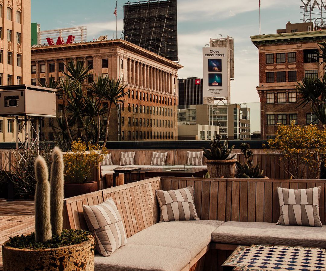 A tan-toned rooftop restaurant with cactus, overlooking a Hollywood skyling.