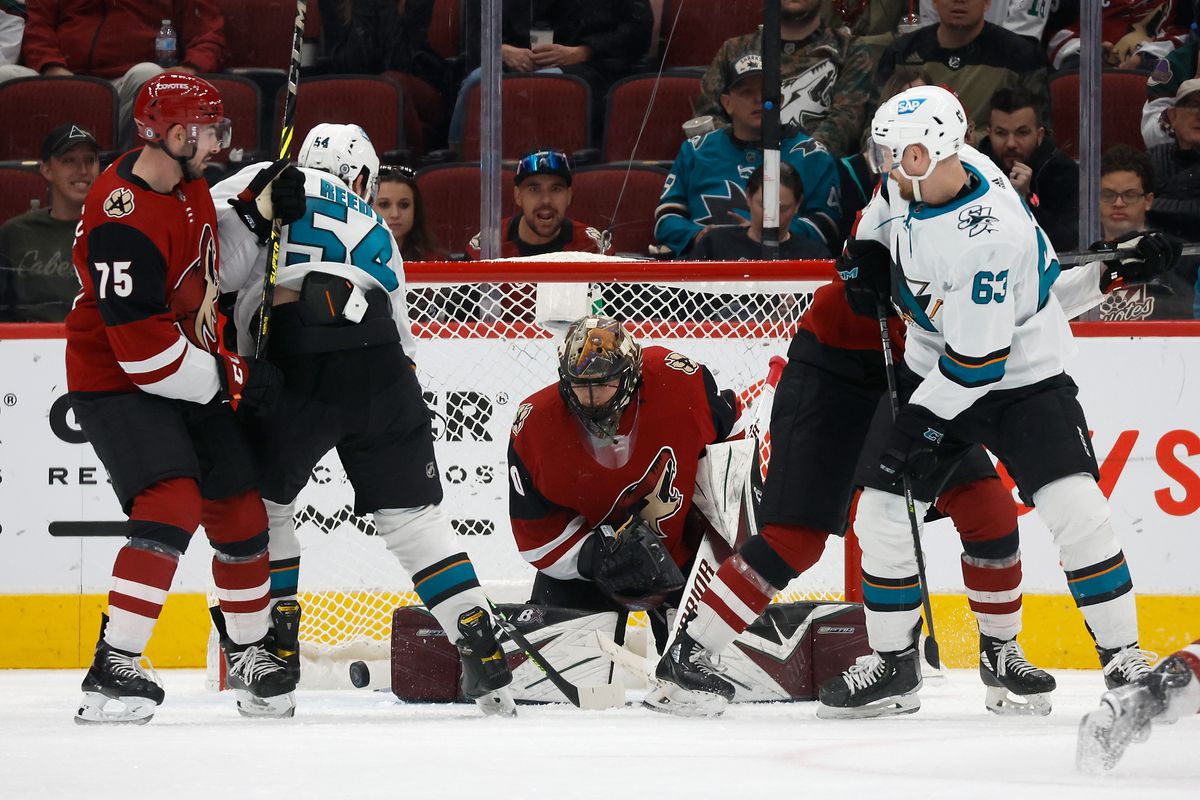 Goaltender Karel Vejmelka #70 of the Arizona Coyotes makes a save on a shot as Scott Reedy #54 and Jeffrey Viel #63 of the San Jose Sharks look for a rebound during the third period of the NHL game at Gila River Arena on March 30, 2022 in Glendale, Arizona.&nbsp;