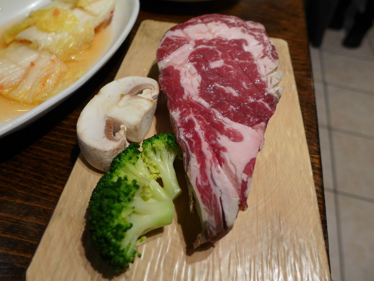 A raw marbled steak with mushrooms and broccoli on the side.