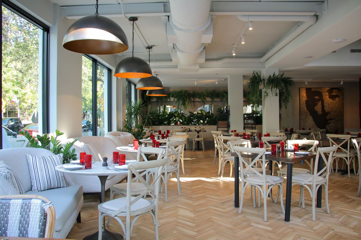 indoor dining area with white chairs, couches, handing chandeliers, white washed wood floors