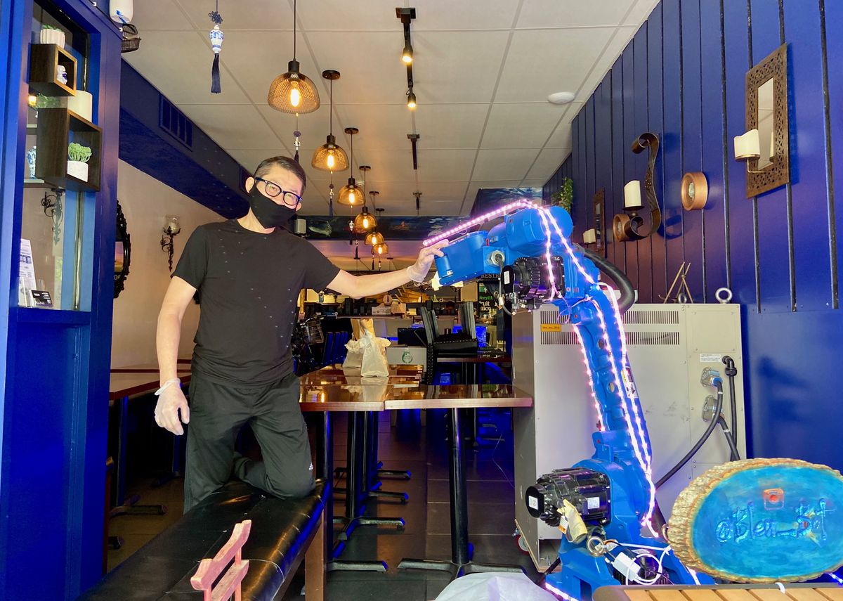 man wearing mask and gloves inside restaurant with blue walls next to mechanical arm