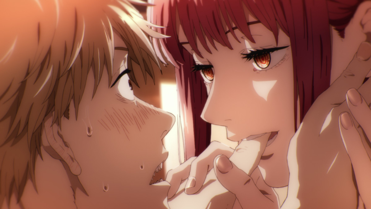 A still from the first trailer of Chainsaw Man, depicting a red-haired anime girl with yellow eyes biting the thumb of a blushing anime boy with light brown hair.
