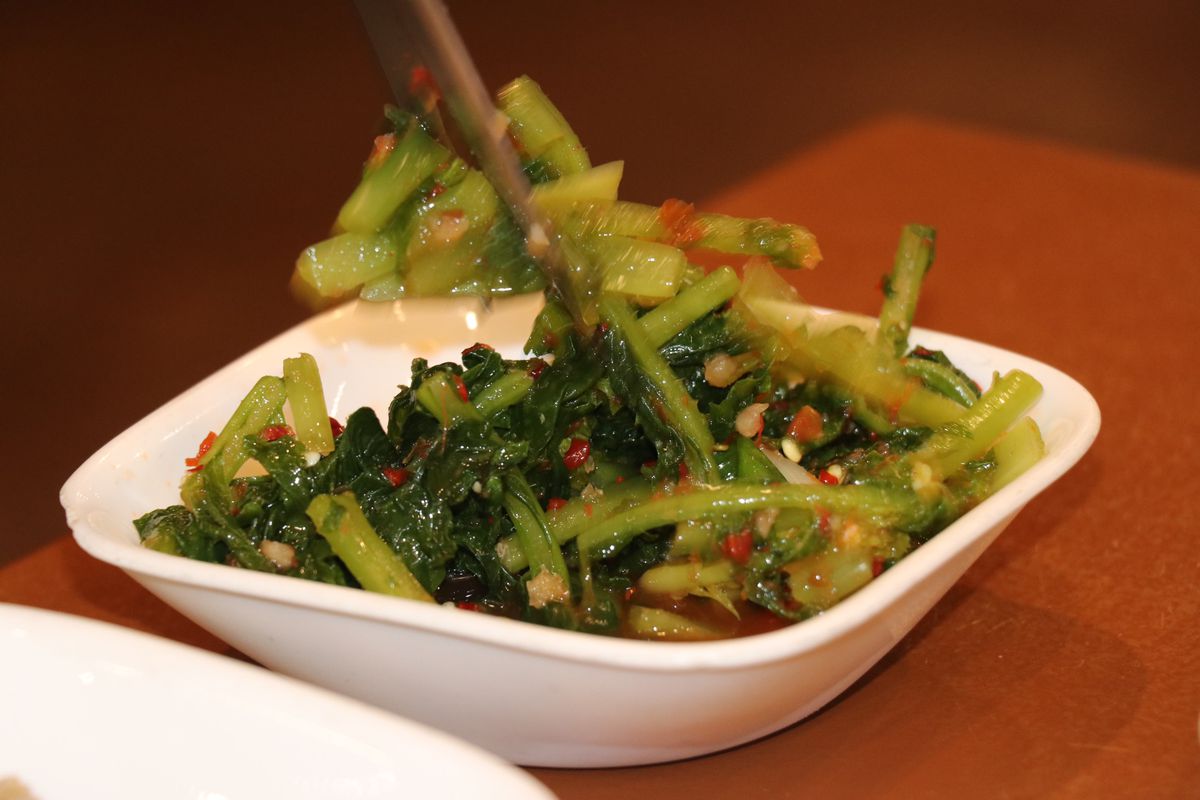 A close-up of pickled greens being picked up by chopsticks. 