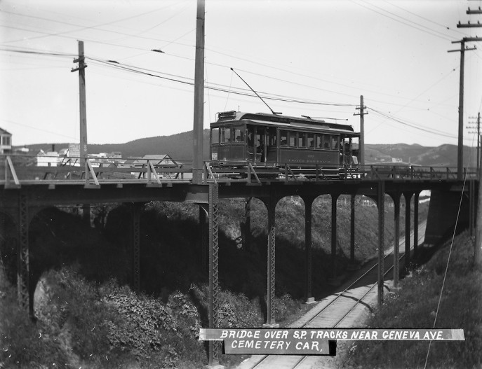 A black and white photo of a streetcar on a bridge over an SF street.