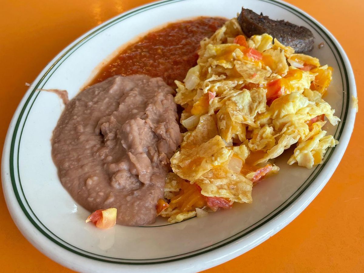 A plate of eggs with chips, refried beans, and red sauce.