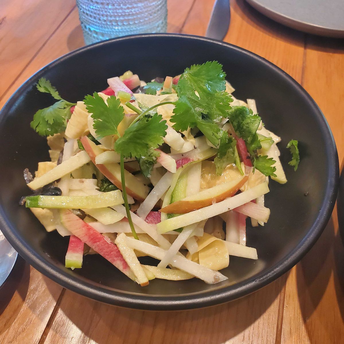 A bowl of yuba salad, with matchstick-sized pieces of cucumber, kohlrabi, apple, and sprigs of cilantro