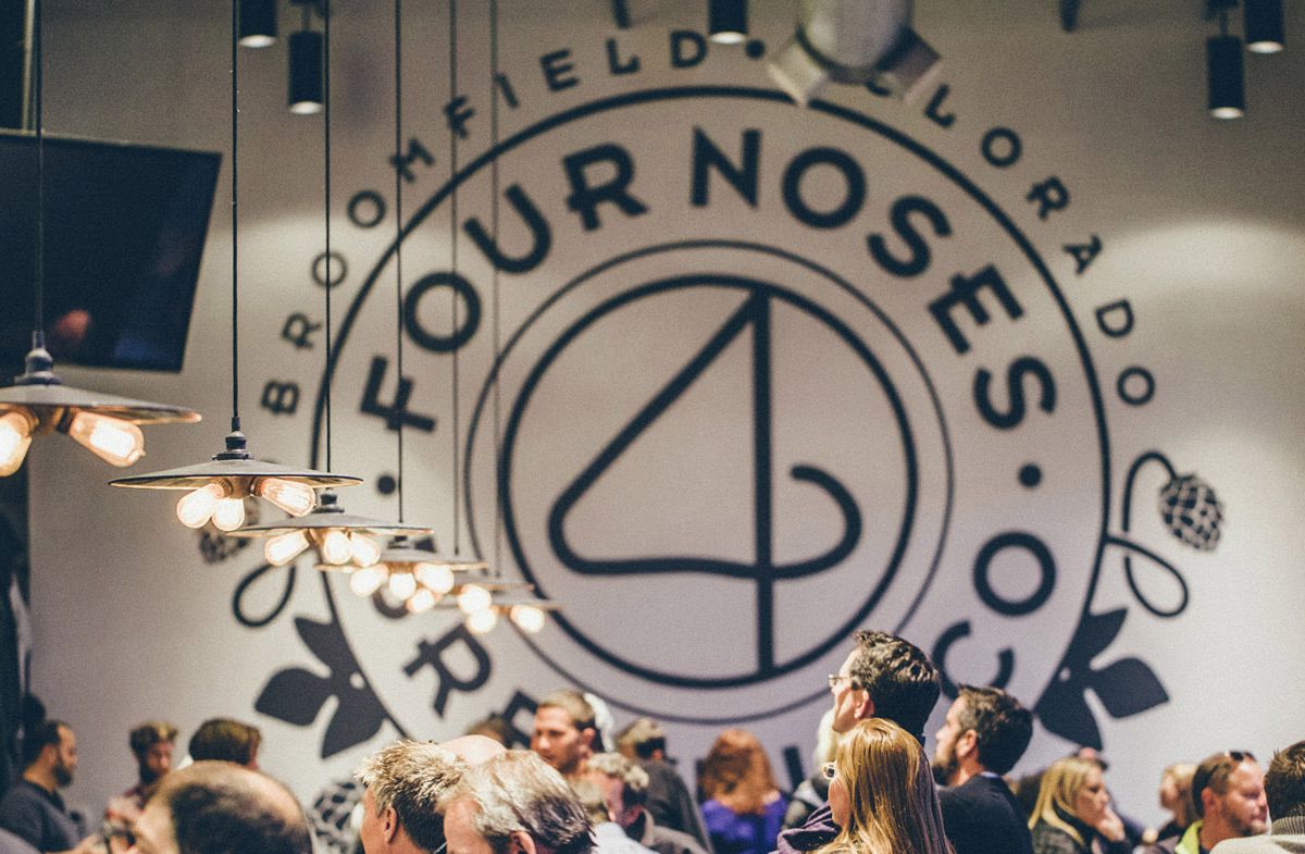 A crowded taproom and a large wall logo at 4 Noses Brewing Company