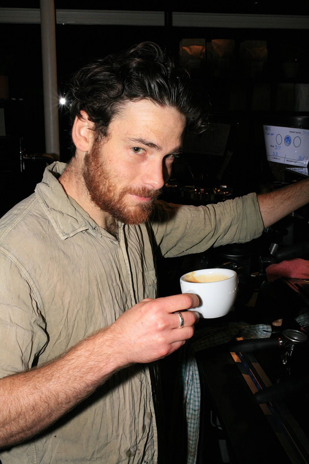 A barista in a beige shirt holds a half-drunk coffee cup.